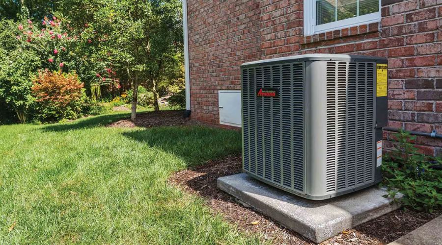 New air conditioner unit installed outside a brick home, surrounded by green grass and landscaping, representing efficient HVAC solutions for improved indoor comfort.